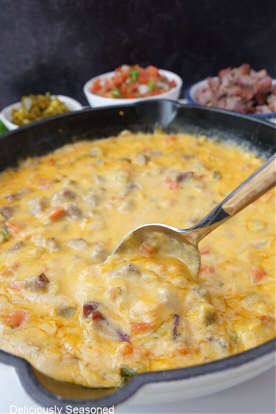 A cast iron skillet filled with queso and a spoon stirring the queso.