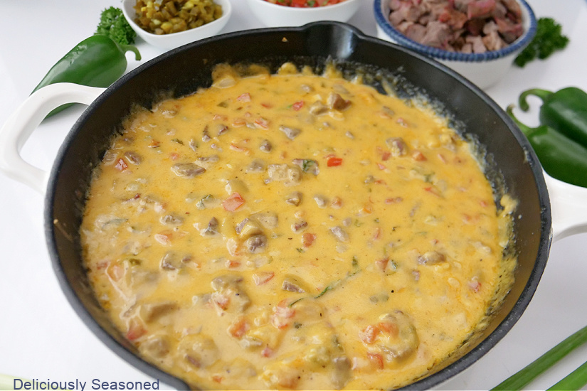 A horizontal photo of brisket queso in a white cast iron skillet.