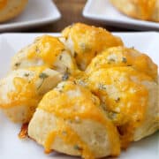 A baked biscuit with cheese and diced jalapenos on a white plate.