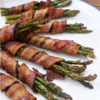 A white plate with eight bunches of asparagus wrapped in bacon.