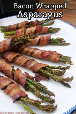 A large white plate with blue trim with 8 cooked asparagus spears wrapped in bacon.