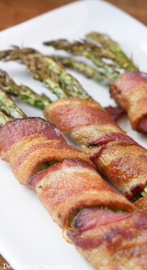 Three asparagus spears with bacon wrapped around them on a white plate.
