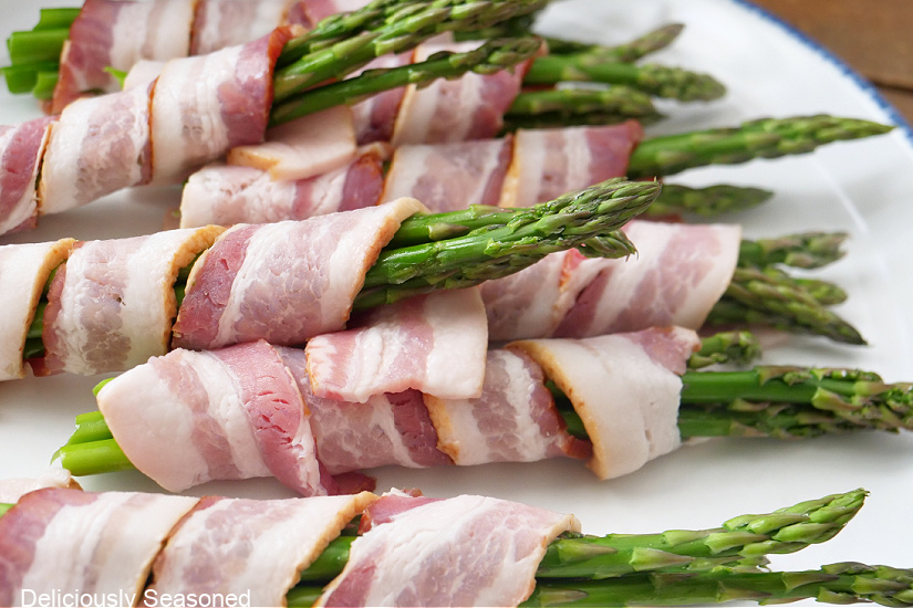 Asparagus wrapped in bacon on a white plate before being put in the air fryer.