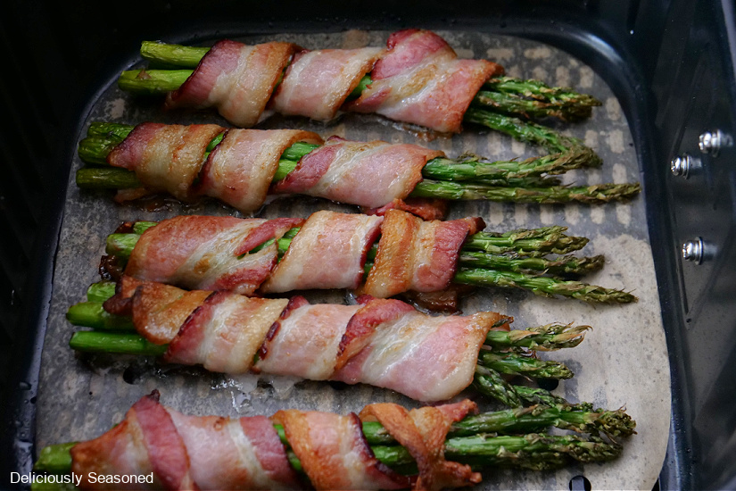 A horizontal photo of five bunches of asparagus and bacon in the air fryer basket.