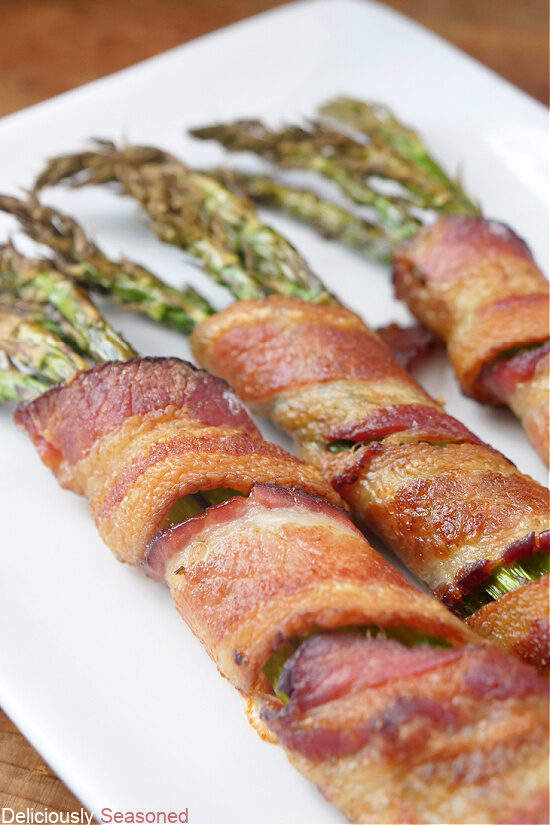 A white plate with three bunches of bacon wrapped asparagus on a white plate.