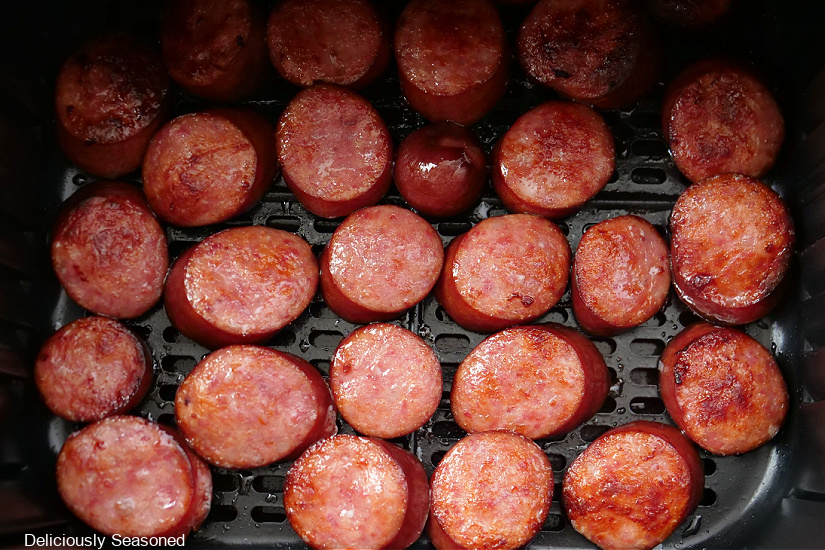 Air fryer basket with sliced smoked sausage in it.