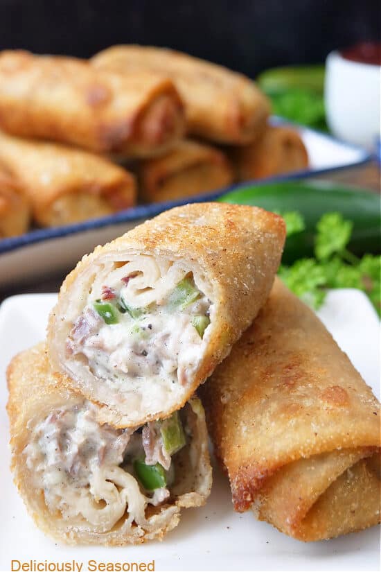 Two egg rolls on a white plate with more egg rolls in the background.