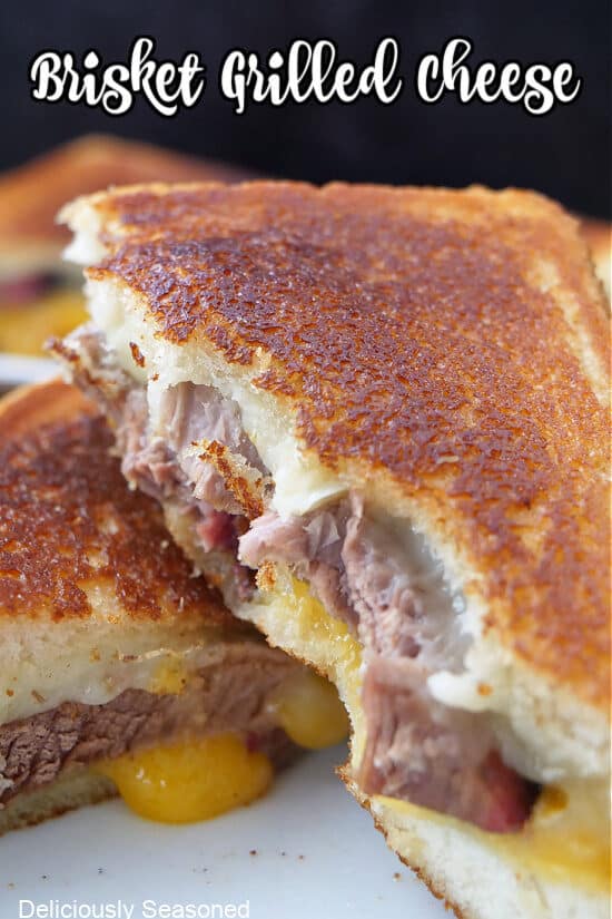 A brisket grilled cheese sandwich cut in half with a bite taken out of it and one half is place on the other half.
