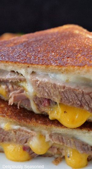 A leftover brisket grilled cheese sandwich cut in half and the two halves are placed on top of each other showing the brisket and melty cheese.