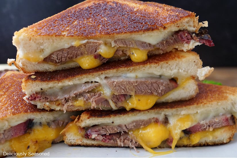 A horizontal photo of two brisket grilled cheese sandwiches that are cut in helf and placed on top of each other.