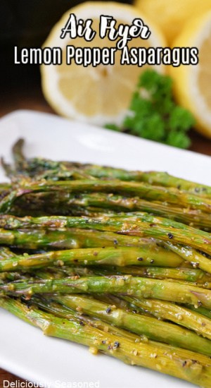A white plate with air fried asparagus on it with lemons in the background.