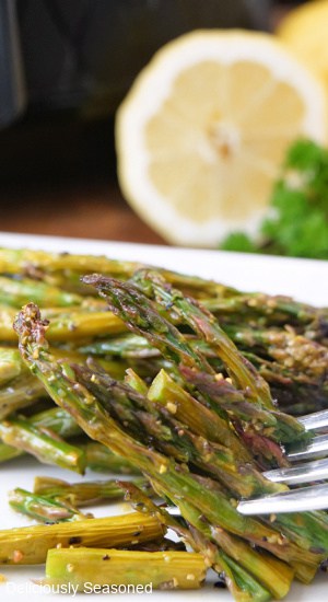 A serving of asparagus on a white plate with a forkful of asparagus.