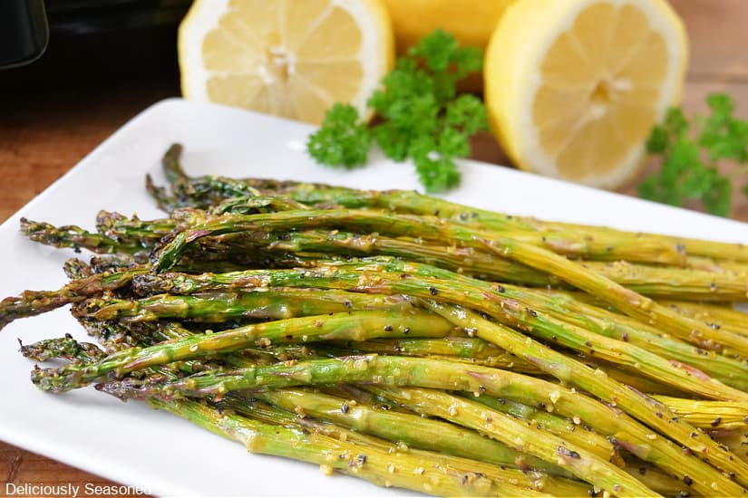 A horizontal photo with lemon pepper asparagus on a white oblong plate after being air fried.