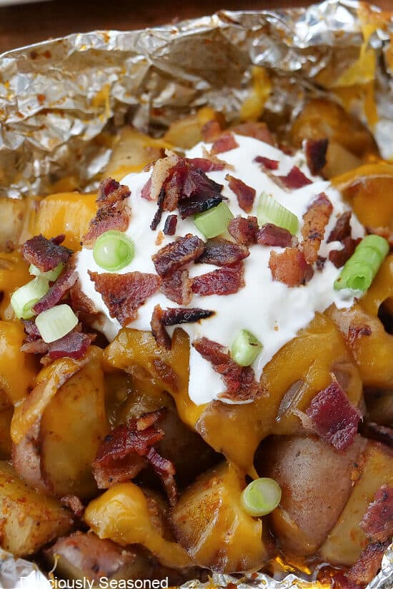 A close up of an opened potato foil packet showing the diced potatoes, sour cream, bacon and green onions.