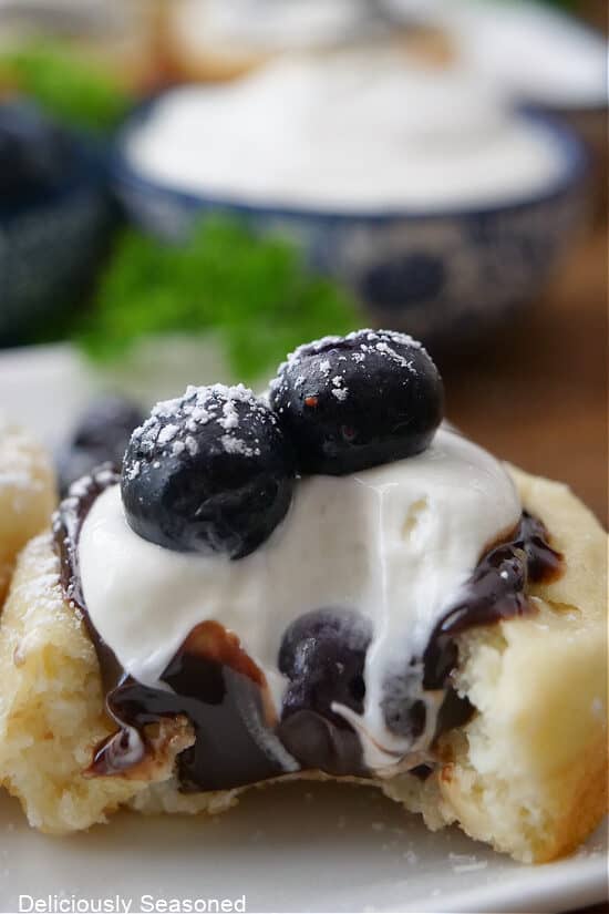 A close up of a pancake cup filled with hot fudge, cream cheese and topped with blueberries that has a bite taken out of it.