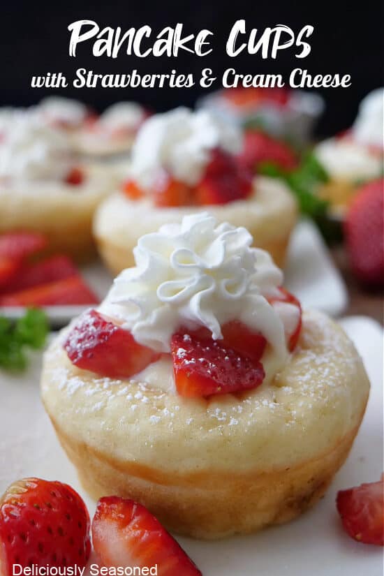 A close up photo of a pancake cup on a white plate filled with cream cheese and topped with strawberries and whipped cream.