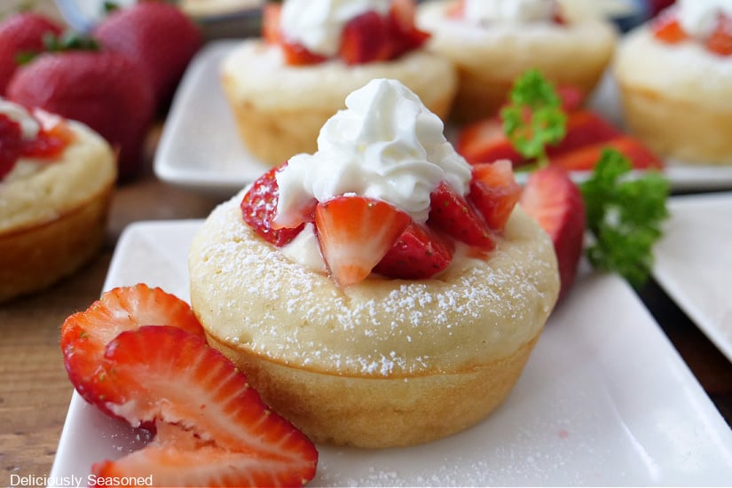 A horizontal photo of a white plate with a pancake cup on it filled with a sweet cream cheese filling and topped with fresh diced strawberries and whipped cream.