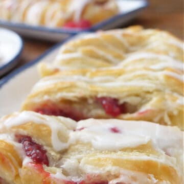 A white plate with blue trim with a raspberry pastry braid on it with another pastry in the background.