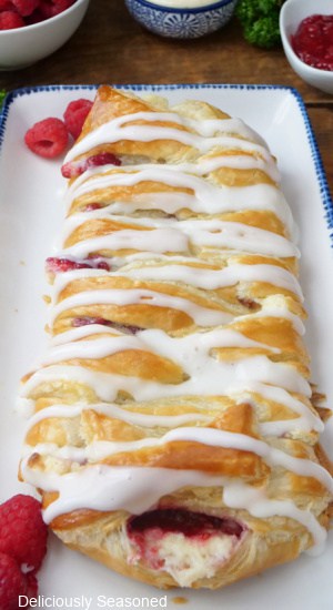 A raspberry pastry braid on a white plate that is drizzled with a sweet glaze.
