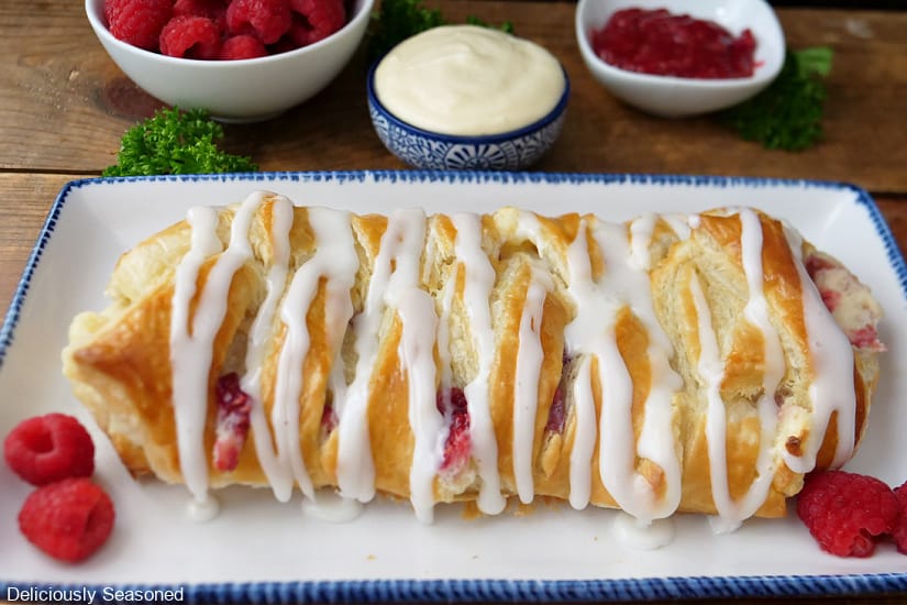 A horizontal photo of a raspberry pastry braid on a white plate with blue trim.