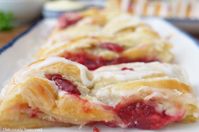 A horizontal photo of a white plate with a pastry braid on it fill with a sweet cream cheese and raspberry filling and drizzled with glaze.