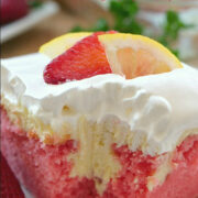 A slice of strawberry cake with a lemonade cream cheese filling and cool whip and a slice of strawberry and lemon on top.