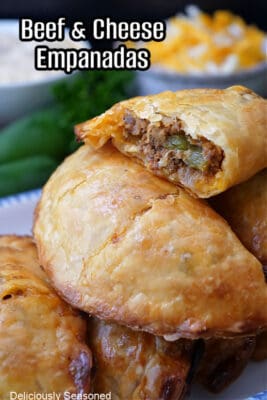 A few beef empanadas on top of each other with one broke in half showing the inside ingredients.