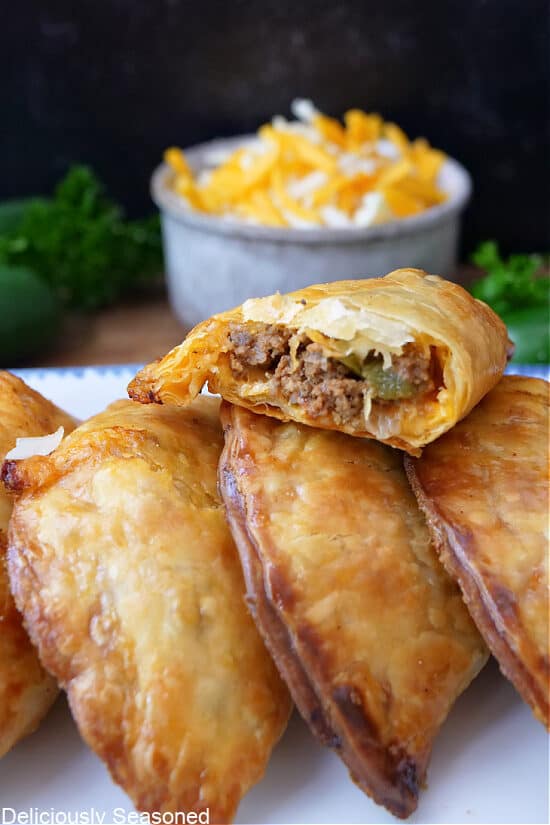 Four golden brown, flaky beef and cheese empanadas on a white plate.