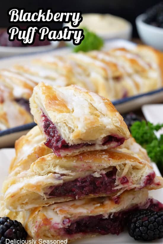 A few slices of blackberry pastry stacked on top of each other with a whole puff pastry braid in the background.