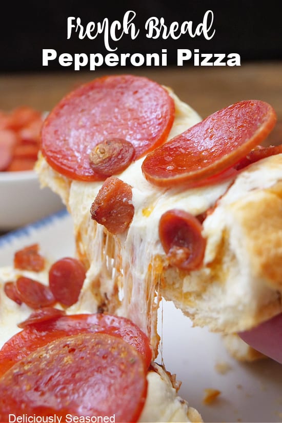 A slice of homemade pizza bread lifted off a white plate showing the stretchy cheese and the different types of pepperonis.