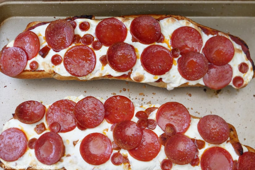 A baking sheet with two halves of French bread pepperoni pizza on it after being removed from the oven before being sliced.