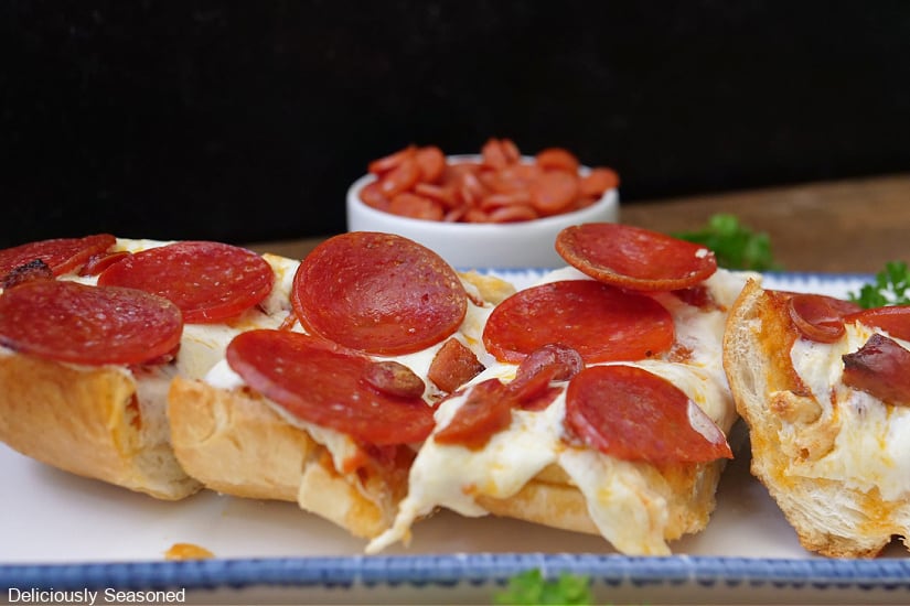 A horizontal photo of a section of French bread pepperoni pizza cut into slices the is loaded with cheese and pepperonis.