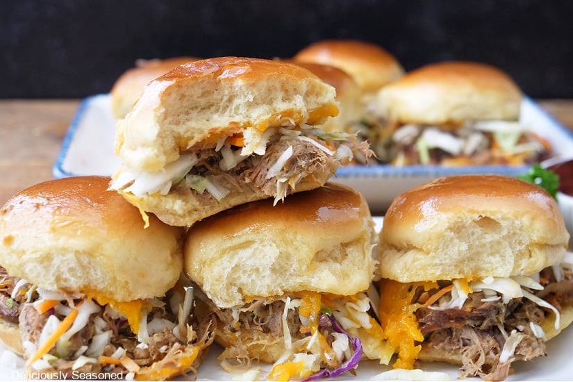 A horizontal photo of 4 pork sliders on a white plate with more sliders in the background.