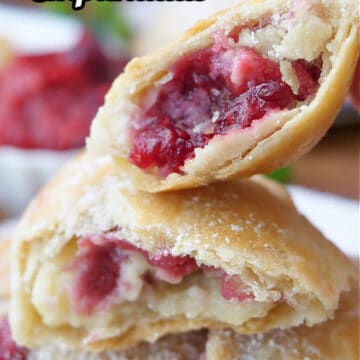 A couple empanadas filled with raspberries and cream cheese, and one of them broke in half showing the inside filling.