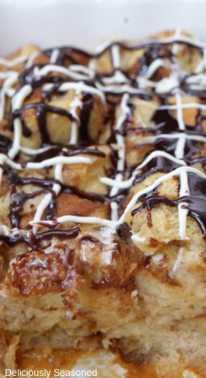 A casserole dish filled with bread pudding drizzled with white and dark chocolate.