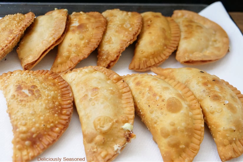 A baking sheet with parchment paper that has 10 fried empanadas on it.