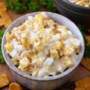 A bowl of hot corn dip with fritos on the table.
