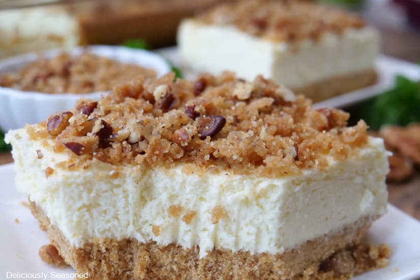 A horizontal photo of a maple cheesecake bar with a crunchy pecan topping that has a bite taken out of it.