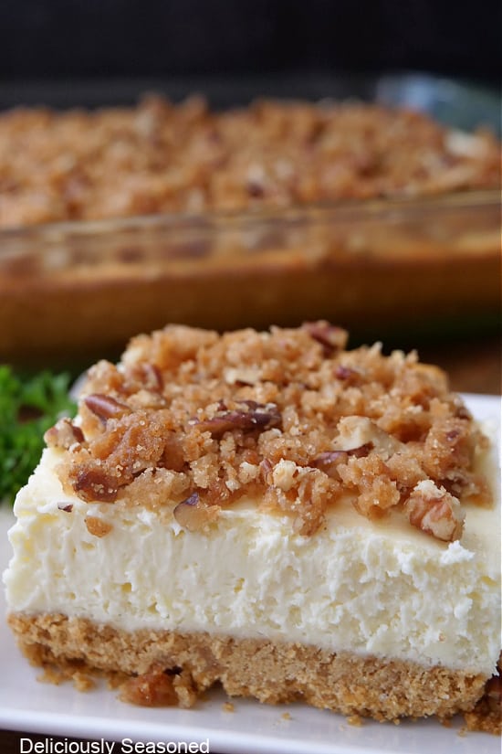 A cheesecake bar on a white plate that has a crunchy pecan crumb topping.