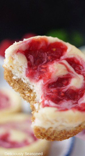 A close up of a little raspberry cheesecake with a bite taken out of it.