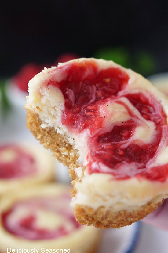 A close up of a mini raspberry cheesecake with a bite taken out of it.