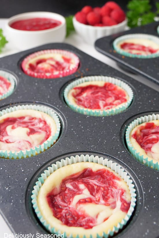 A muffin pan with little cheesecakes in them after being pulled out of the oven.