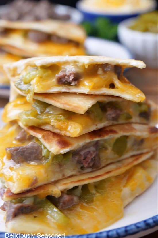 A stack of cheese, steak, and chile quesadillas on a white plate with blue trim.