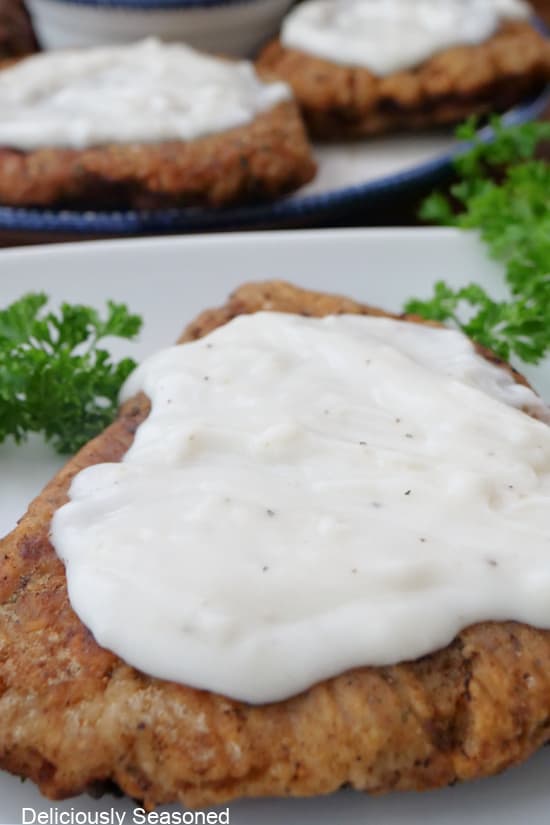 A close up of a serving of chicken fried steak with gravy on top placed on a white plate.