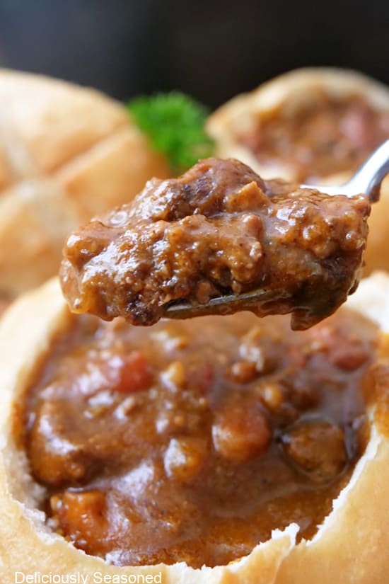 A spoonful of chili with a bread bowl filled with chili.