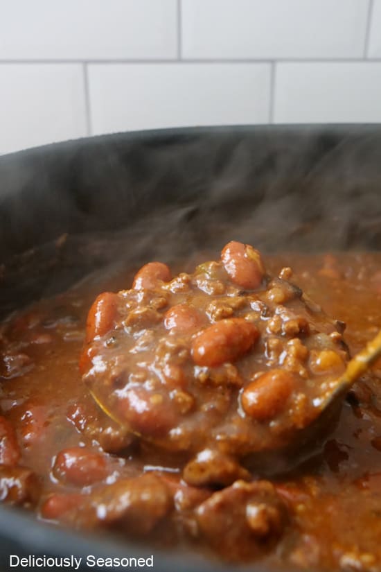 A black Dutch oven with a ladle filled with chuck roast chili.