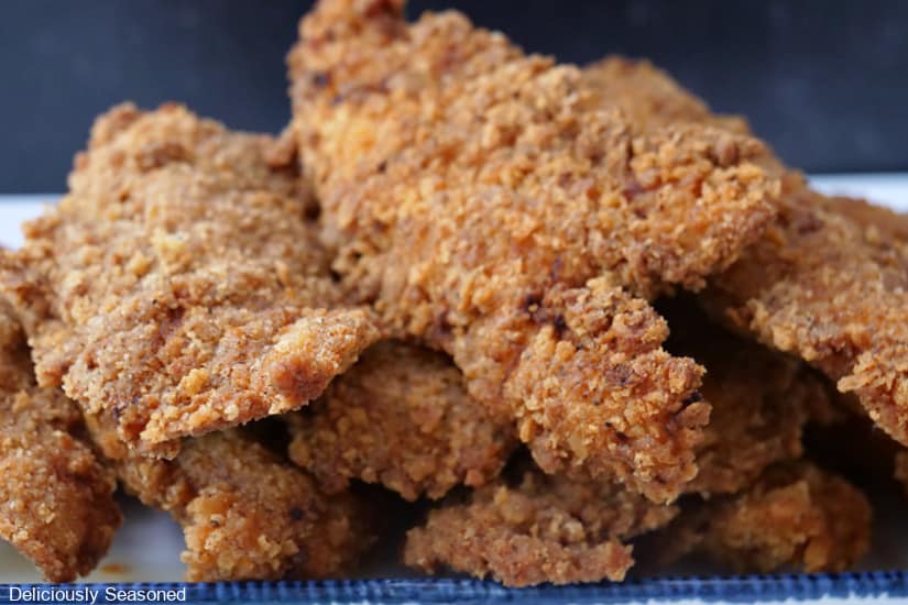 A horizontal photo of a stack of chicken strips on a white plate with blue trim.