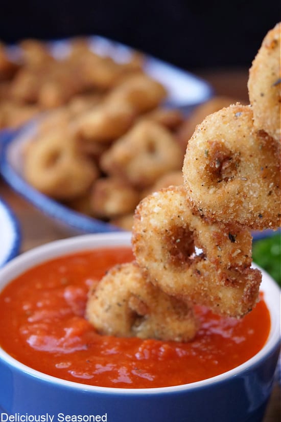 A blue bowl filled with marinara sauce with fried tortellini being dipped into it.
