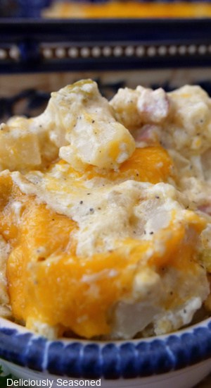 A close up of a serving of hash brown casserole in a white bowl with blue trim.