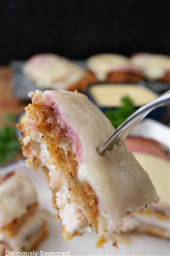 A close up of a bite of chicken topped with ham and Swiss cheese on a fork.